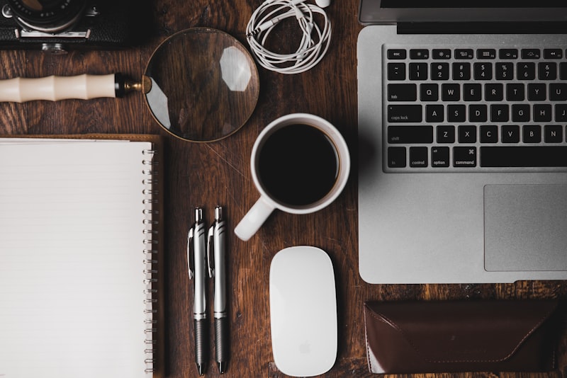 A notebook and pen on a wooden table beside a cup of coffee.